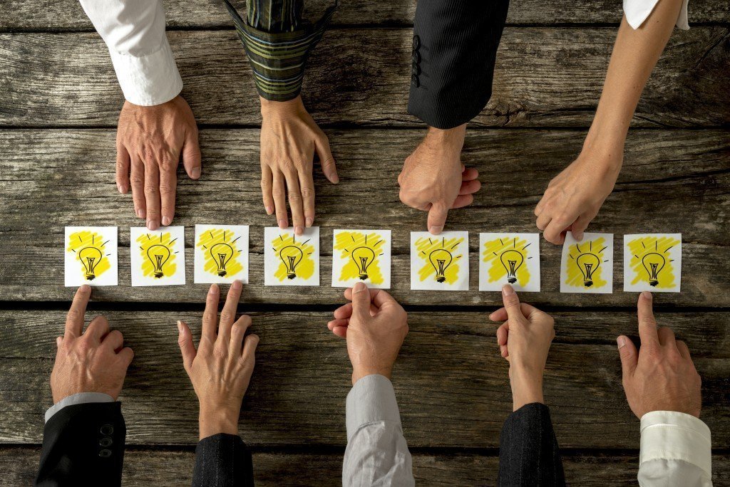 Hands of diverse individuals reaching toward the center, touching cards with idea icons, symbolizing collaboration and brainstorming in customer journey mapping.